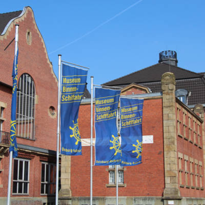 Blaue Fahnen vor dem roten Backsteingebäude des Binnenschifffahrtsmuseum Duisburg
