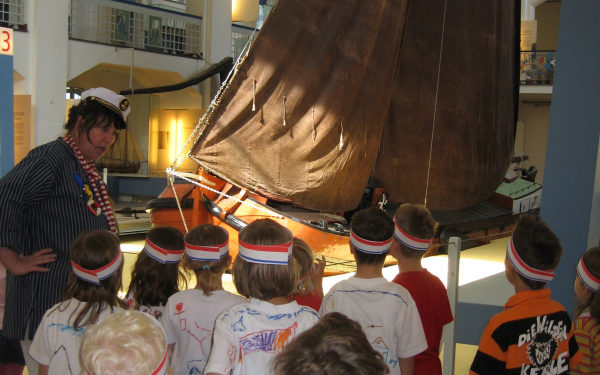 Kinder stehen vor einem Schiff mit Mast im Binnenschifffahrtsmuseum Duisburg